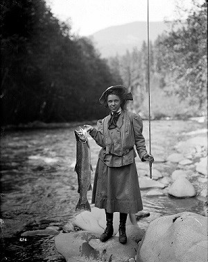 Historic photograph of a woman holding a salmon beside the Elwha River